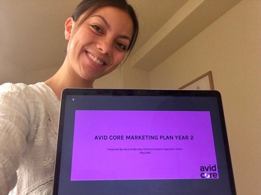 Spring intern, Hana Chabinsky, smiles for a selfie and shows the title page of her marketing plan.