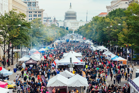 Patrons walking through various tented food stands on a narrow street. The United States Capitol sits at the end of the street.