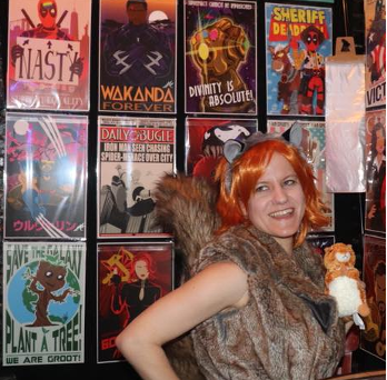 Woman dressed in an orange wig with gray and black headband featuring animal ears, and a brown, furry vest stands in front of a wall covered in Marvel comic book covers.