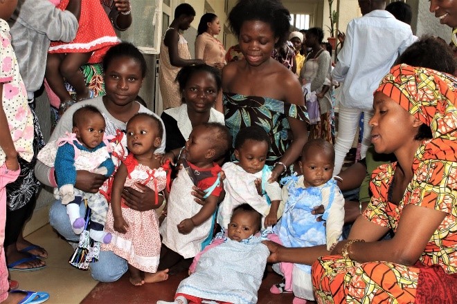 A group of Black children with Black women holding them pose for a picture.