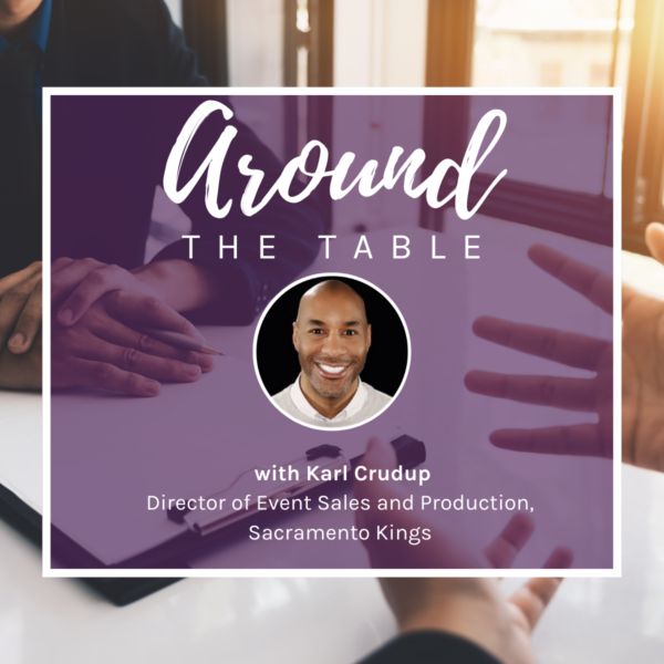 The background picture is of two individuals sitting across from each other at a table. The image is focused on their hands, and one has a clipboard resting underneath their hands on the table. Over the picture, is a purple square with a white border. The heading reads, “Around the Table.” Beneath the heading, is a circular headshot of Rodney Gaines. Underneath the headshot reads, “with Karl Crudup, Director of Event Sales and Production, Sacramento Kings"",” in white text.