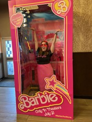 Ashley, wearing a pink outfit, poses inside a large, faux-Barbie box at the movie theater.