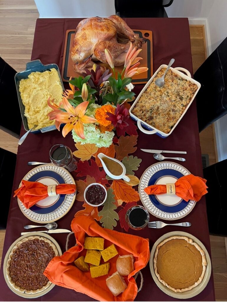 A Thanksgiving dinner for two with turkey, pies, creamy mashed potatoes, and dressings on a decorated table seen from above.