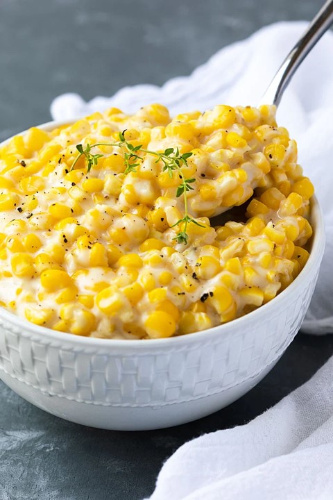 A bowl of creamed corn, with a spoon dipping into the bowl.