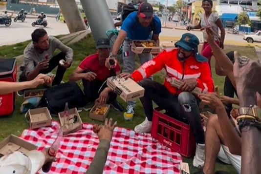 A group of unhoused individuals share a meal sitting on the grass.