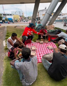 A group of unhoused individuals share a meal sitting on the grass.